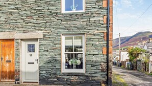 A stone building with a wooden door, a white door, and a window with a plant inside. - 2 Bed in Keswick (oc-93224) (Keswick)
