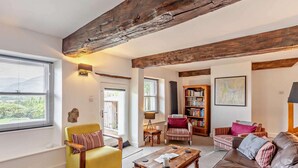 A living room with a yellow armchair, a brown leather sofa, a wooden coffee table, a bookshelf, and exposed wooden beams on the ceiling. - 3 Bed in Underskiddaw (oc-sz377) (Underskiddaw)