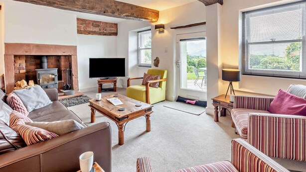 A living room with a fireplace, sofas, a television, and a view through a window. - 3 Bed in Underskiddaw (oc-sz377) (Underskiddaw)