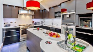 A modern kitchen with a central island, stainless steel appliances, and red pendant lighting. - 3 Bed in Underskiddaw (oc-sz377) (Underskiddaw)