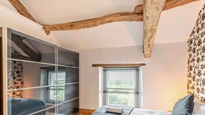 A bedroom with a bed, a wardrobe, a window, and a wooden ceiling beam. - 3 Bed in Underskiddaw (oc-sz377) (Underskiddaw)