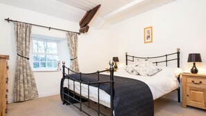 A bedroom with a metal bed frame, a wooden nightstand, a bedside table, a window with curtains, and a picture on the wall. - 2 Bed in Keswick (oc-sz330) (Saint John's Castlerigg and Wythburn)