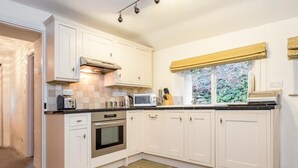 Una cocina con gabinetes blancos, un microondas, un tostador y una ventana con un adorno amarillo.