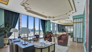 En rymlig hotellobby med en receptionsdisk, en sittgrupp, stora fönster och utsikt över stadens silhuett.