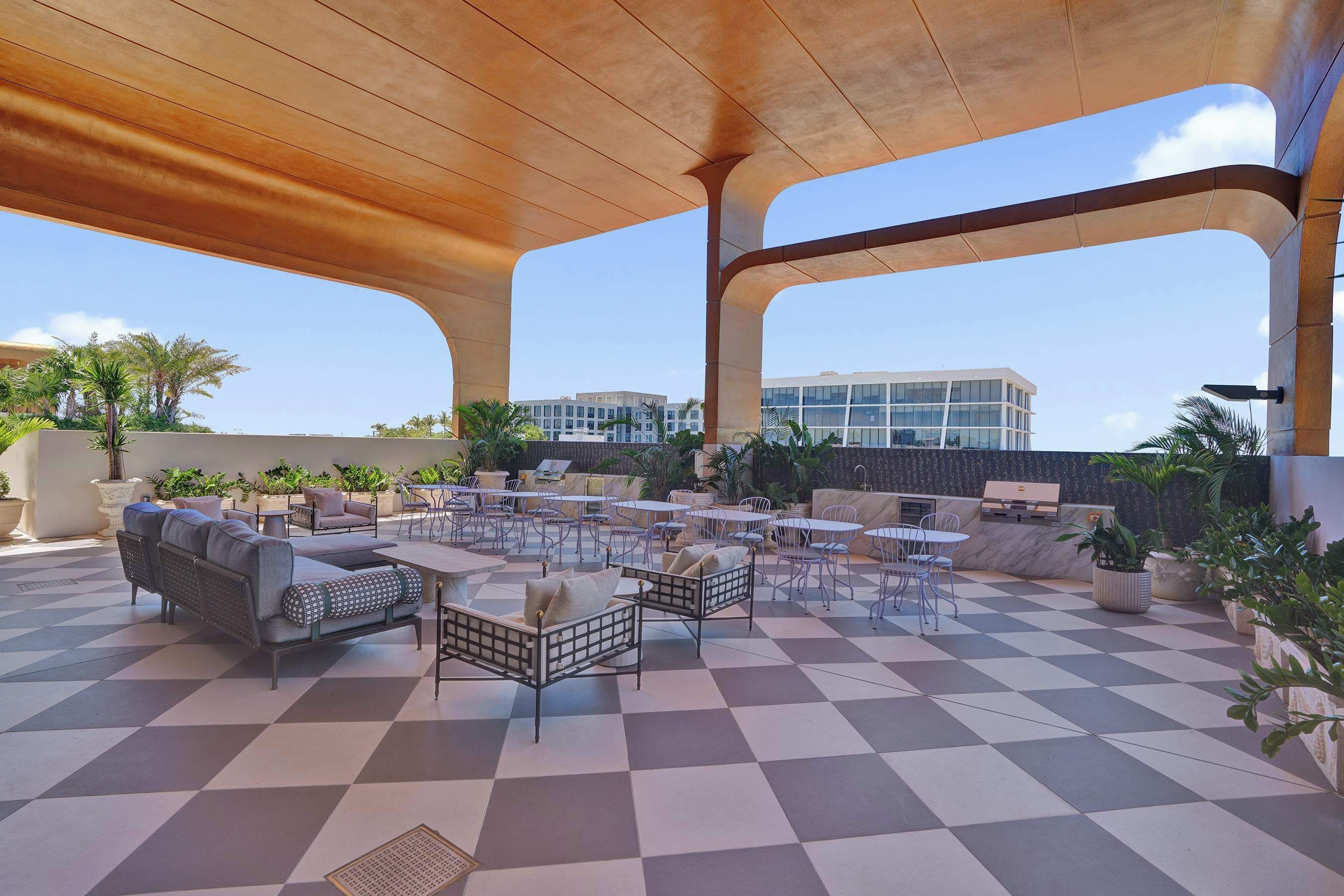 A rooftop terrace with outdoor seating, a checkered floor, and a view of buildings in the background.