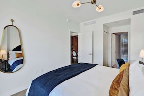 Habitació d'hotel amb un llit, un mirall, una làmpada al sostre i una porta oberta que dona a un bany.
