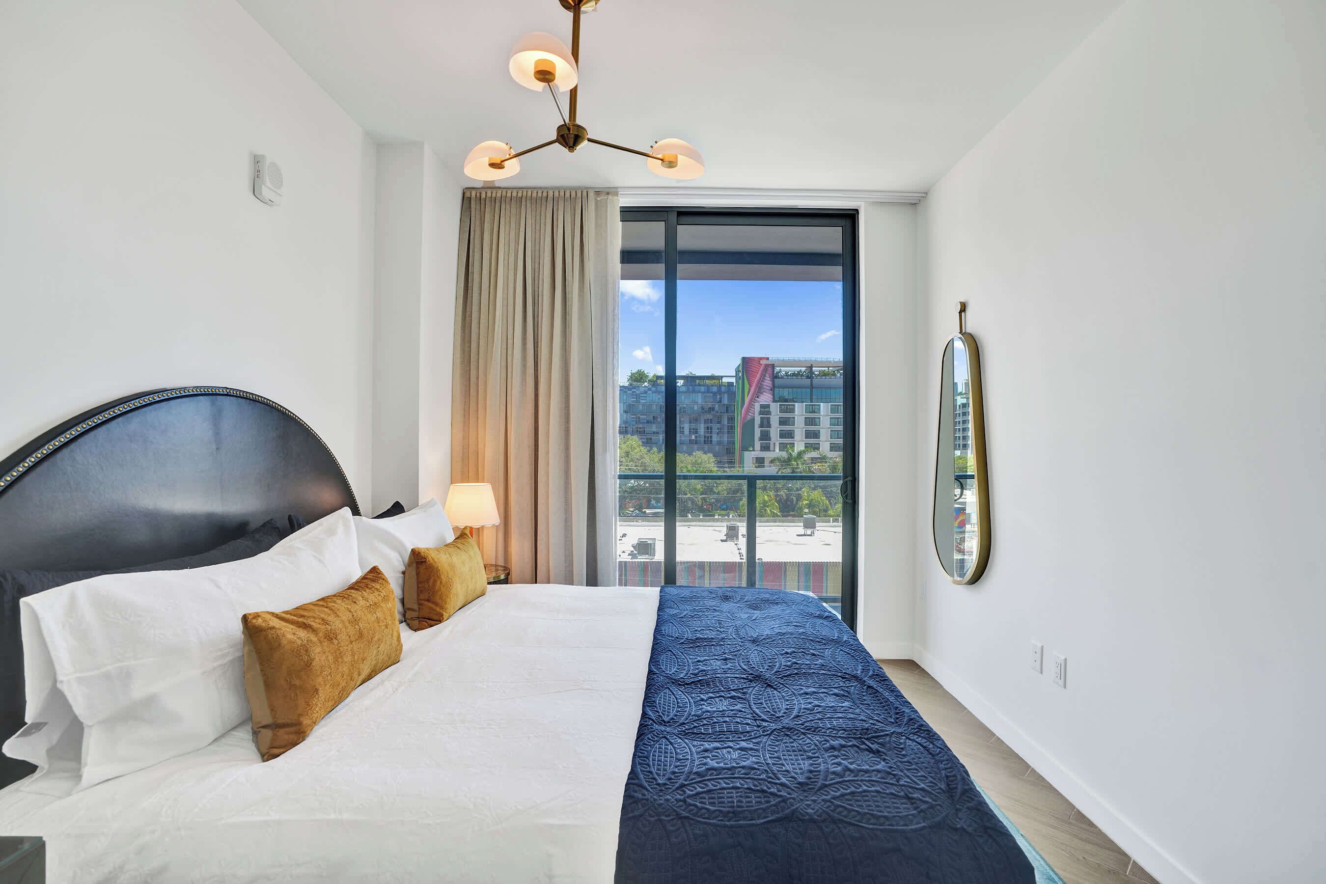 Une chambre d’hôtel avec un grand lit, une vue par une porte coulissante, un lustre et un miroir au mur.