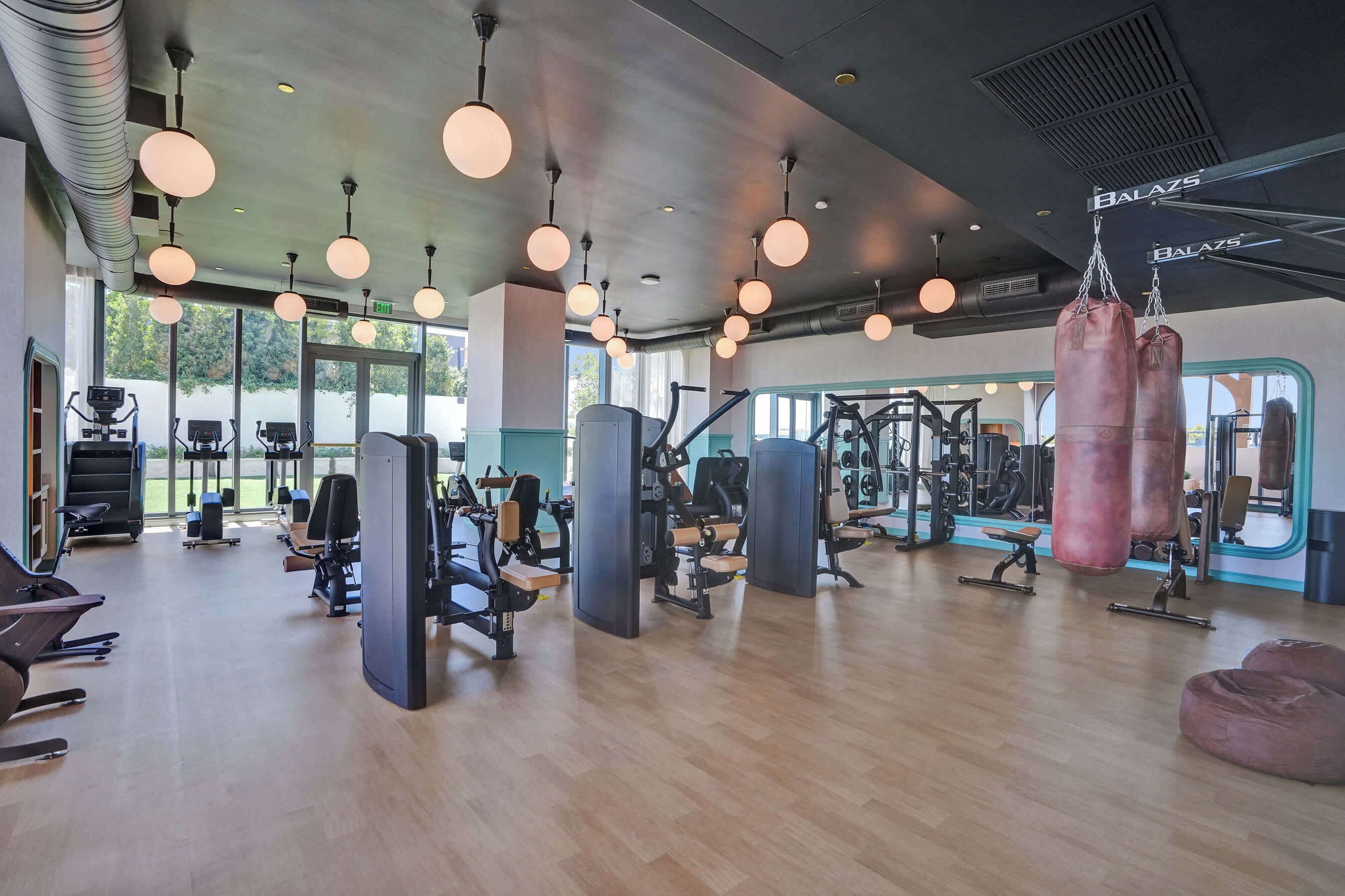 Ein Fitnessstudio mit Trainingsgeräten, großen Fenstern und hängenden Lampen.