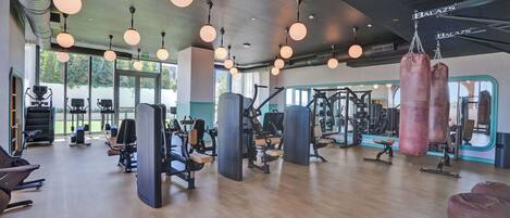 Ein Fitnessstudio mit Trainingsgeräten, großen Fenstern und hängenden Lampen.