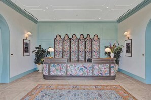 A reception area with a decorative counter, wall-mounted lamps, framed pictures, and potted plants. - Nomad (Miami)