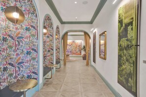 A hallway with patterned wallpaper, a tiled floor, and framed artwork on the walls. - Nomad (Miami)