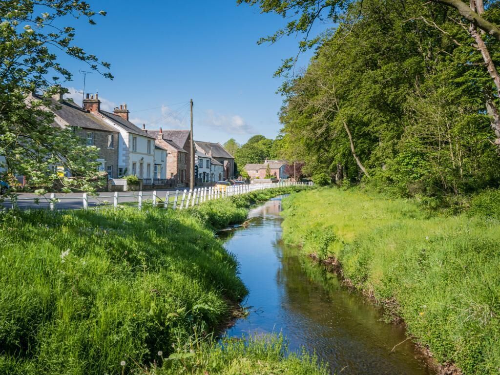 A narrow waterway flanked by lush greenery and traditional stone houses with white fences.