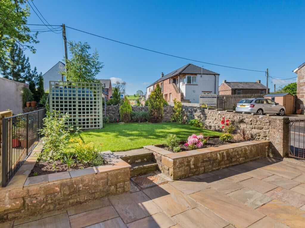 Ein Wohnhaus mit Pflasterpatio, umzäunter Garten und einer Steinmauer.