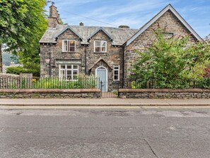 A stone house with a gabled roof, a front door, and a small garden area. - 3 Bed in Keswick (oc-sz542) (Keswick)