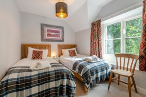 A bedroom with two beds, a wooden chair, a window with curtains, and a hanging light fixture. - 3 Bed in Keswick (oc-sz542) (Keswick)