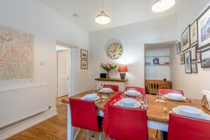 A dining area with a wooden table set for four, red chairs, a wall clock, and a map on the wall. - 3 Bed in Keswick (oc-sz542) (Keswick)