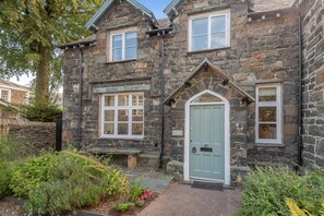 A stone house with a central door, two windows on the upper floor, and a small porch area. - 3 Bed in Keswick (oc-sz542) (Keswick)