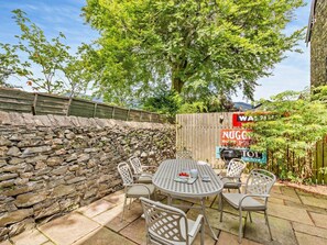 A patio with a stone wall, a round metal table, and white chairs. - 3 Bed in Keswick (oc-sz542) (Keswick)