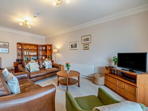 A living room with a brown leather sofa, a green armchair, a wooden coffee table, a television, and a bookshelf. - 3 Bed in Ambleside (oc-82119) (Claife)