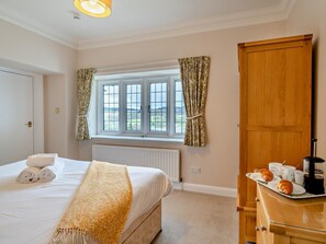 A bedroom with a bed, a radiator, a window with curtains, a wooden wardrobe, and a breakfast tray with croissants and coffee. - 3 Bed in Ambleside (oc-82119) (Claife)