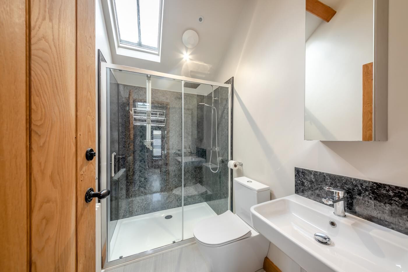 A modern bathroom with a glass-enclosed shower, a white toilet, and a sink with a marble countertop.