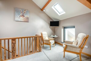 Ein Zimmer mit Holzbalkon, zwei Stühle, einem kleinen Tisch, einem Bild, einem Fernseher und einem Fenster.