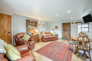 A living room with leather sofas, a dining table with chairs, a wooden cabinet, and a mounted television. - 1 Bed in Cleator (oc-92310) (Ennerdale and Kinniside)