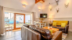 A furnished living room with a leather sofa, a wooden coffee table, and a television mounted on the wall. - 3 Bed in Cleator (oc-88627) (Ennerdale and Kinniside)