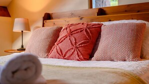 A neatly made bed with a patterned pillow and a rolled towel, a bedside lamp, and a window with a view of greenery. - 3 Bed in Cleator (oc-88627) (Ennerdale and Kinniside)