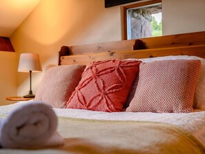 A neatly made bed with a patterned pillow and a rolled towel, a bedside lamp, and a window with a view of greenery. - 3 Bed in Cleator (oc-88627) (Ennerdale and Kinniside)