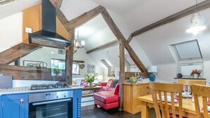 Et moderne køkken med en blå komfur, træbjælker og et spiseområde med en rød stol og et træbord.