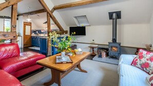 En hyggelig stue med pejs, et spiseområde med en rød lædersofa, og et køkken i baggrunden.