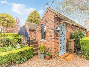 A brick house with a blue door, a welcome mat, and a small garden with potted plants. - 2 Bed in Kidderminster (oc-cc090) (Neen Sollars)
