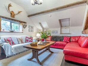 A cozy living room with a red sofa, a white sofa with floral cushions, a wooden coffee table, and a ceiling-mounted deer head decoration. - 2 Bed in Kidderminster (oc-cc090) (Neen Sollars)