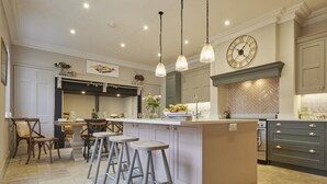 Una cocina con una isla central, taburetes de bar, luces colgantes y un reloj en la pared.