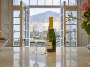 Una ampolla de xampany Taittinger, dues flautes i un bol de fruita sobre una taula amb vistes a les muntanyes a través de grans finestres.