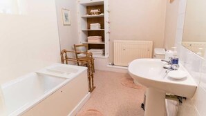 A bathroom with a bathtub, a sink, a radiator, and a shelf with folded towels. - 3 Bed in Cockermouth (SZ022) (Cockermouth)