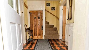 A hallway with a checkered floor, a wooden door, a staircase, and a small table with a chair. - 3 Bed in Cockermouth (SZ022) (Cockermouth)