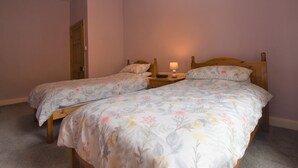 A bedroom with two single beds, a nightstand with a lamp, and a door. - 3 Bed in Cockermouth (SZ022) (Cockermouth)
