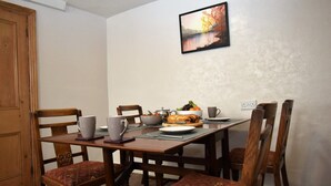 A dining area with a table set for four, including a bowl of fruit, a loaf of bread, and a cup. - 3 Bed in Cockermouth (SZ022) (Cockermouth)