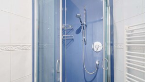 Ducha con cerramiento de vidrio, cabezal de ducha manual, grifo empotrado y panel de control.