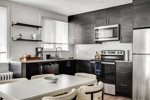 A modern kitchen with a central island, built-in appliances, and a dining area with a white table and chairs. - Downtown Ottawa | Modern APT (Ottawa)