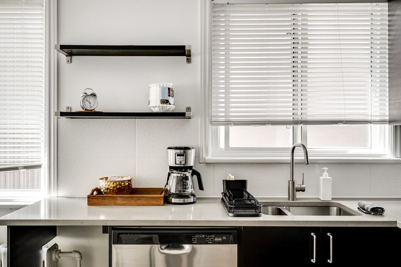 Una cocina con cafetera, lavaplatos y fregadero.
