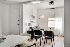 A modern living room with a white sofa, a dining table with chairs, a floor lamp, and a window with curtains. - Downtown Ottawa | Modern APT (Ottawa)