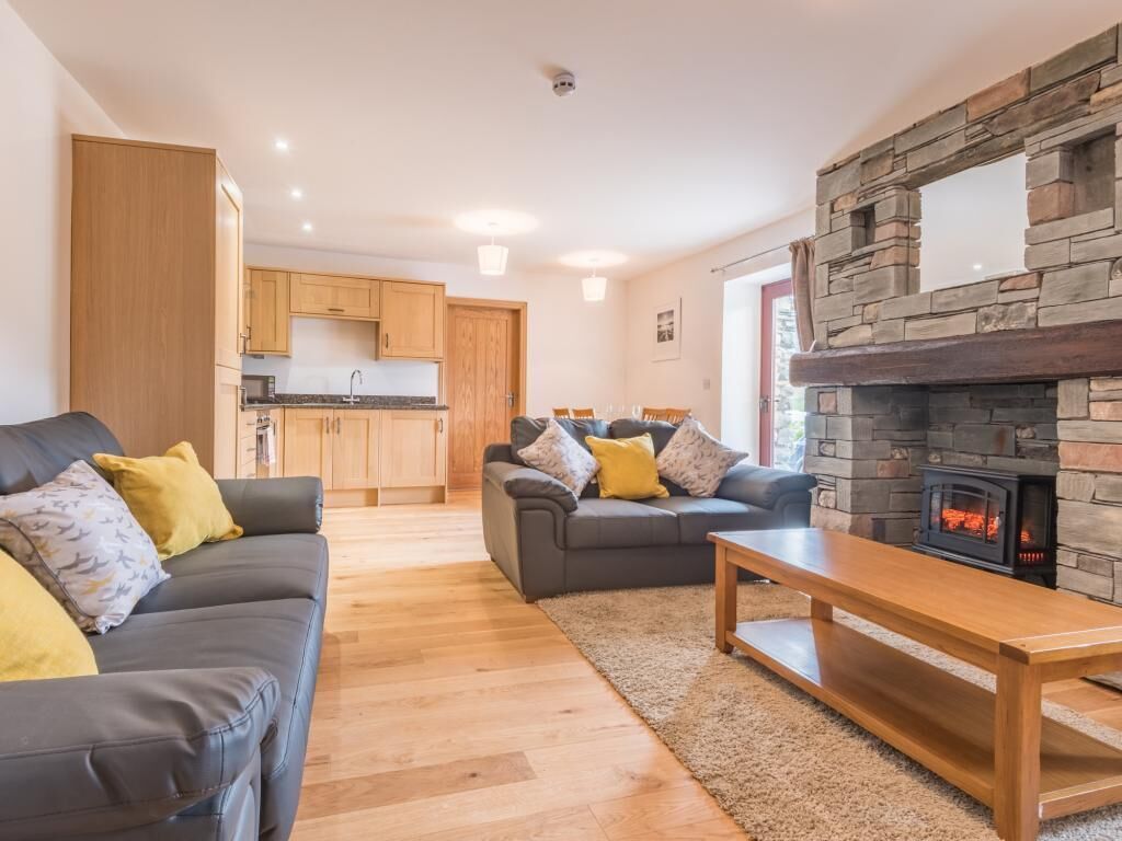 A modern living room with a fireplace, a sofa, a dining table, and a kitchen in the background.