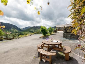 A picnic table with benches, a stone building, and a mountainous landscape in the background. - 2 Bed in Newlands Valley (SZ351) (Borrowdale)