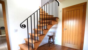 Eine Holztreppe mit schwarzen Geländern, ein runder weißer Gegenstand auf einem Hocker und eine Holztür.