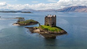 Ein historischer Steinturm auf einer kleinen Insel, umgeben von ruhigem Wasser, mit Bergen in der Ferne unter einem teilweise bewölkten Himmel.