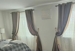 A bedroom with a bed, curtains, a wall-mounted light, and a sign. - 4-Bedroom Group Stay • Free Parking (Ottawa)