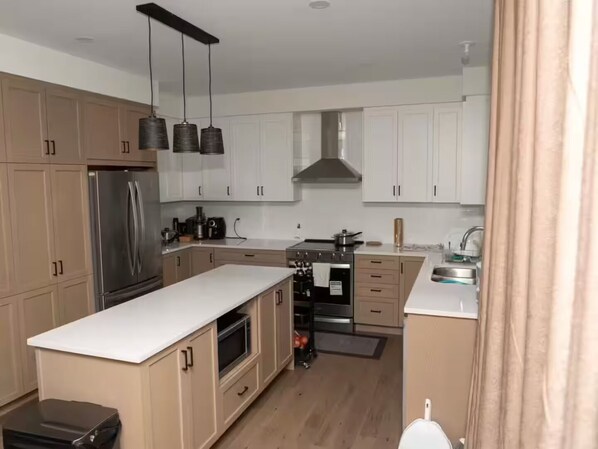 A modern kitchen with wooden cabinets, a stainless steel refrigerator, a gas stove, and hanging pendant lights.
